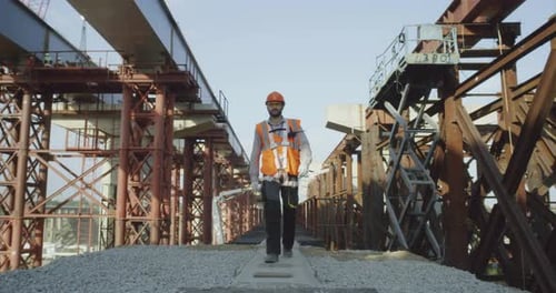 Construction Worker Walking Along Steel Bridge Talking on Radio