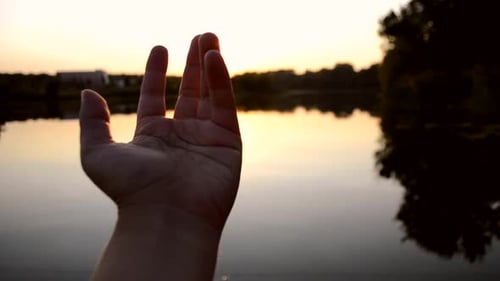 Black Silhouette of Hand Moves It in Air Through Fingers Through Rays of Sun