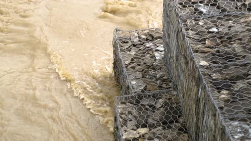 Tidal erosion and flood protection barrier made of cobble stones and metal net. Strengthening