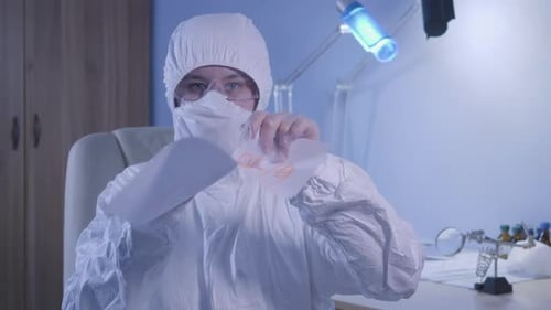 Retrato de una doctora caucásica seria en traje protector rasgando una hoja de papel con Covid-19