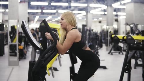 Young Attractive Blond Woman Breathing Intensly While Pedaling on Elliptical Trainer Simulator in