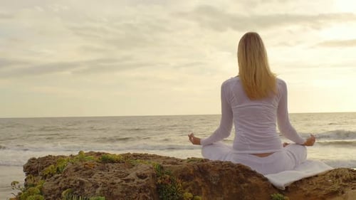Young woman practicing yoga on the beach at sunset