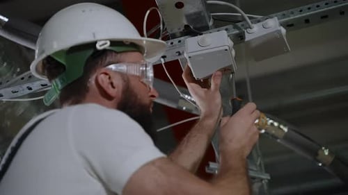 Worker is Repairing Electrical System in Plant Workshop Installing Junction Box
