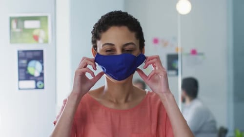 Portrait of caucasian woman adjusting her face mask at modern office
