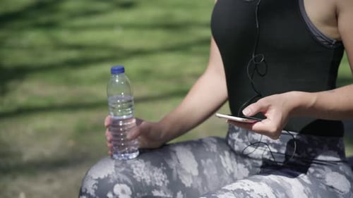 Woman Relaxing with Water and Phone in Park