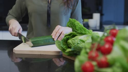 Woman Slicing Cucumber for Salad in Kitchen