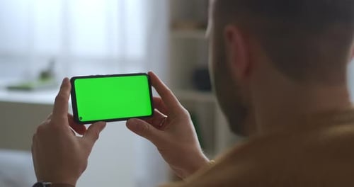 Man Is Viewing on Green Screen of Mobile Phone Holding Horizontally Modern Gadget and App for