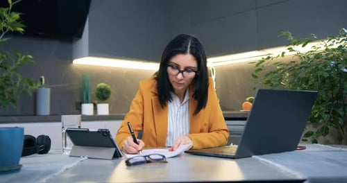 Empresaria con ropa formal sentada en casa en la cocina y revisando documentos
