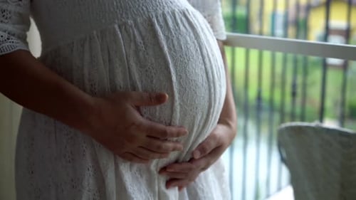 Pregnant Woman Holding Belly in a White Dress