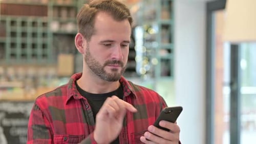 Man Celebrates Good News on Smartphone Indoors