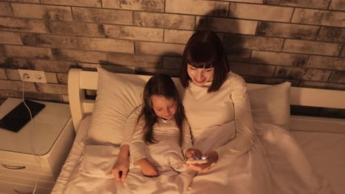 Mother and Daughter Cozy in Bed Using Phone