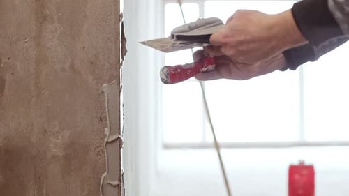 Person Applying Gray Plaster to Wall with Tools