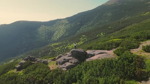 Woman Standing on a Rock with Arms Raised From Aerial View