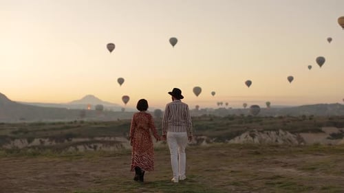 Couple Holding Hands at Sunrise with Hot Air Balloons