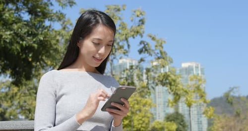 Woman Using Smartphone in City Park on Sunny Day