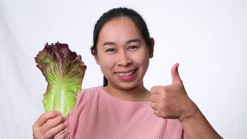 Healthy Asian woman with fresh salad showing thumbs up on white background in studio.
