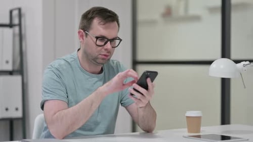 Attraktiver junger Mann mit Smartphone bei der Arbeit