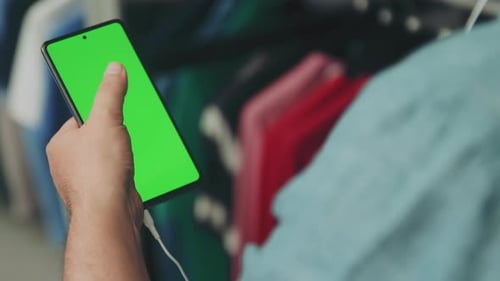 Homme en chemise à l'aide d'un téléphone portable avec écran vert défilant à travers l'affichage tout en regardant et L