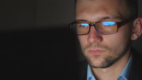 Close Up Male Face of Manager in Eyeglasses with Reflection of Screen Lights Working on Laptop Late