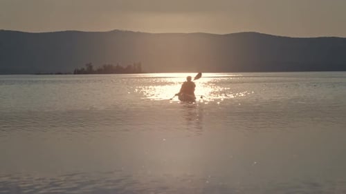 Kayaker Paddles on Calm Lake at Sunset