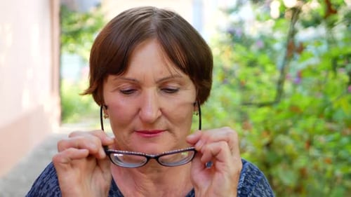 Mature Woman Puts on Stylish Reading Glasses