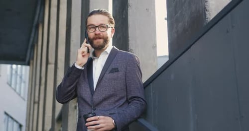 Man in Stylish Suit and Glasses Leaning on the Building Wall and Talking on Smartphone