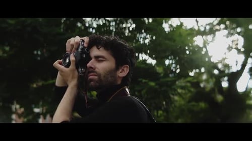 Young Man Takes Pictures with Film Camera in Park