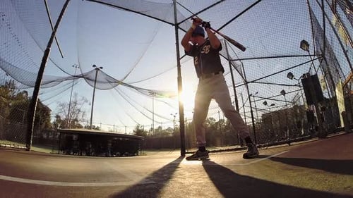 A baseball player practicing at the batting cages.