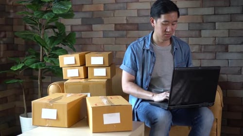 Man Types on Laptop Next to Boxes
