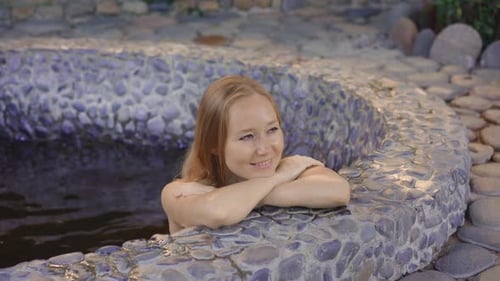 Young Woman Relaxes in a Stone Bath Filled with Healing Herbal Infusions