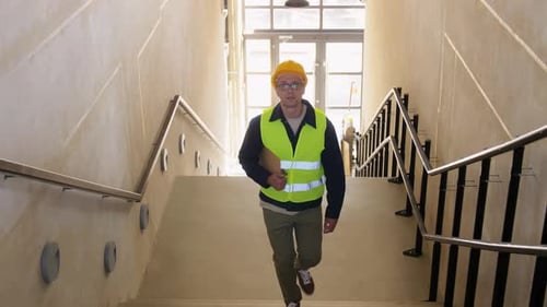 Construction Worker Walks Up Stairs with Blueprints