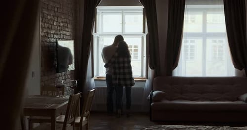 Romantic Couple Embracing by Window in Dim Apartment