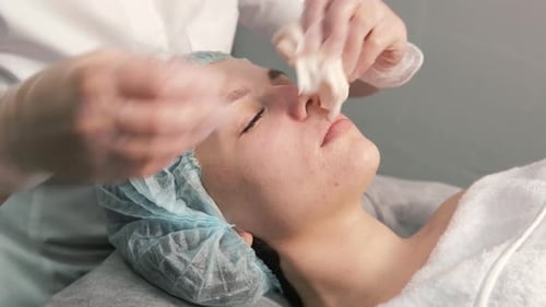 Aesthetician Cleaning Young Woman's Face