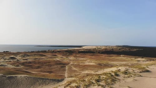 AERIAL: flying over sunny sand dunes towards the sea in the evening