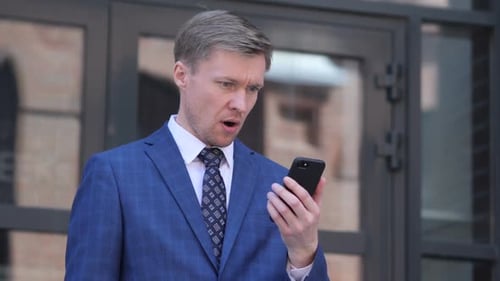 Man Looks at Phone in Disbelief Outside