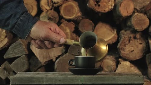Coffee Poured into Black Cup with Logs in Background