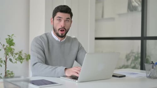 Junger Mann fühlt sich schockiert, als er Laptop im Büro benutzt
