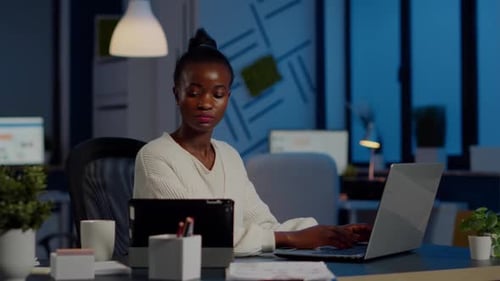 Femme d'affaires noire multitâche travaillant sur ordinateur portable et tablette en même temps
