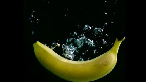 El
plátano cae al agua en cámara lenta. Aislado sobre fondo negro con alfa. Vista de cerca
