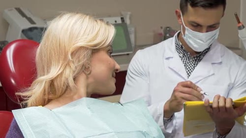 Glückliche Patientin zeigt Daumen hoch sitzend im Zahnarztstuhl bei den Zahnärzten