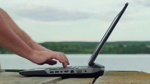 Männerhände benutzen Laptop. Junger Mann benutzt Laptop auf dem Pier.