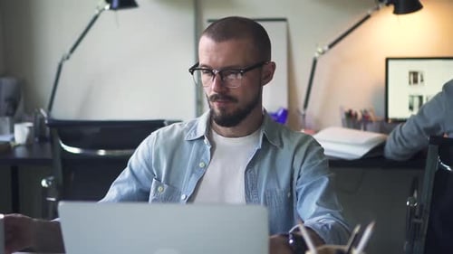 Junger kaukasischer Geschäftsmann arbeitet mit Computer und trinkt Kaffee am Arbeitsplatz im Büro