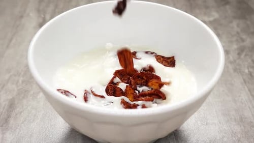 Cornflakes with Chocolate Flavor are Flying From Above Into a White Dish Full of Milk in Slowmo