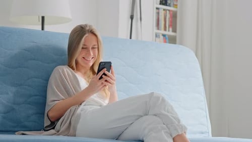 Woman Smiling and Using Mobile Phone on Couch