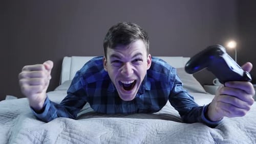 Excited Young Adult Man Playing Video Game in Bedroom