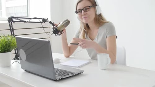 Concept of Streaming and Broadcasting. Young Cheerful Girl in the Studio Speaks Into a Microphone