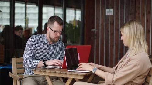 Young Lady and Handsome Guy Are Sitting at Table in Open Cafe Work with Laptops