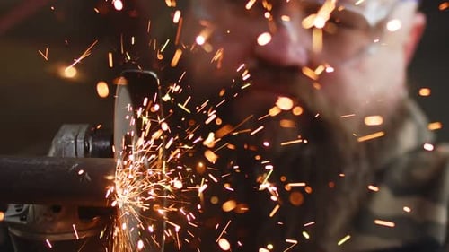 Male Construction Worker in Protective Glasses Works By Cutting Metal Pipe with an Angle Grinder