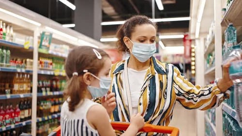 Happy Family in Masks Shopping in the Supermarket Mother and Daughter Buy Mineral Water in a Plastic