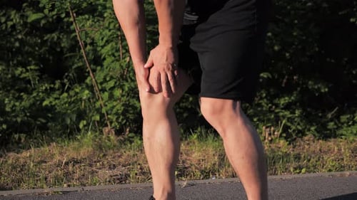 Asian Athlete Male Having Painful Knee Injury During Jogging Exercise in Park